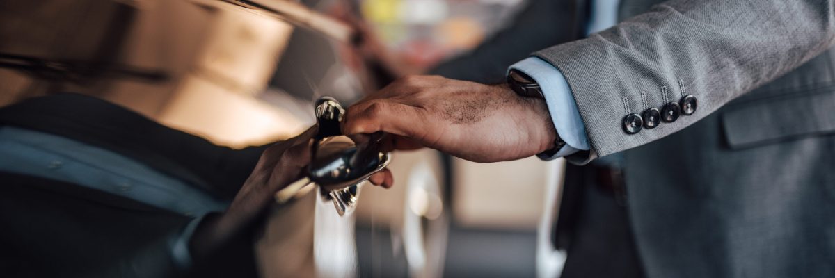 A male in a suit opens the door of his new car.