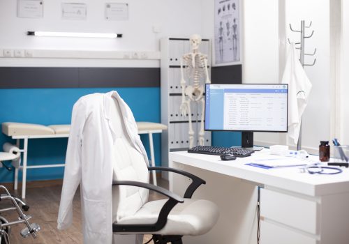 Empty medical office with no people inside, having clinical equipment and computer ready for healthcare use. Modern desktop pc in vacant hospital room displaying patient diagnostic data.
