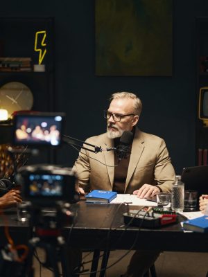 People sitting at table with microphones and talking to writer about his book during podcast