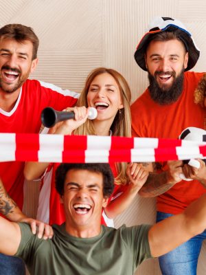 Group of cheerful football fans in sports jerseys with cheering props getting ready for world championship game